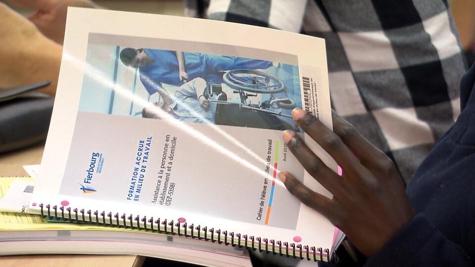 Une élève feuillette un manuel scolaire sur la formation de préposé aux bénéficiaires.