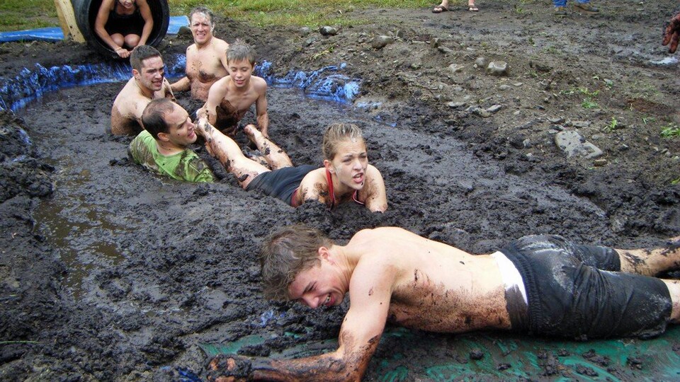 Une équipe composée d'adultes et d'enfants traverse un large carré de boue.