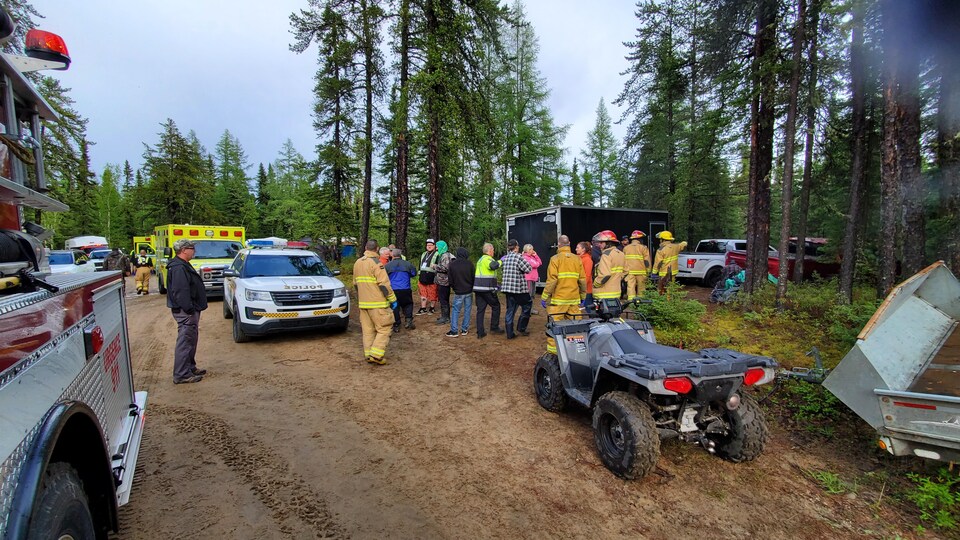 Firefighters were talking to citizens on a dirty forest road.  They are surrounded by emergency vehicles.
