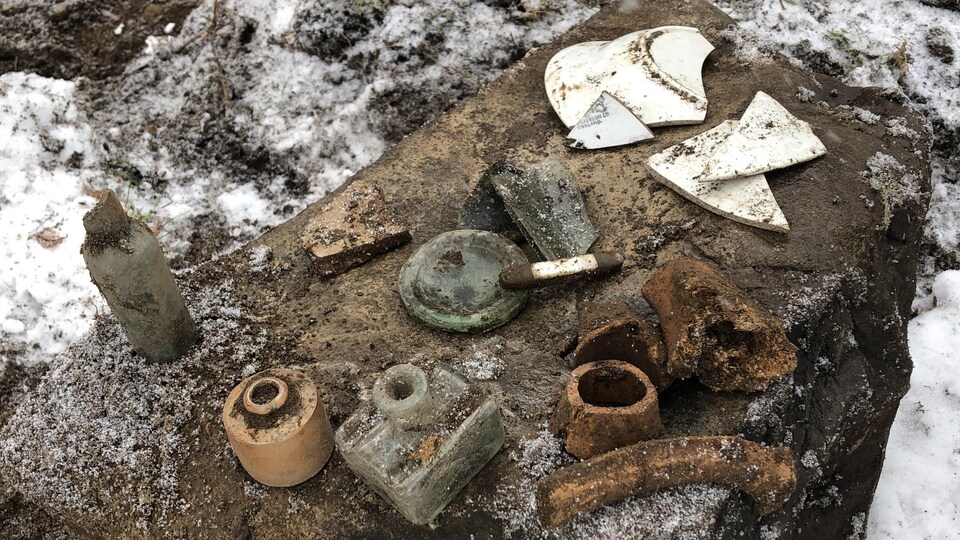 Des morceaux de vaisselle et d'autres objets recouverts de terre sont déposés sur une roche.