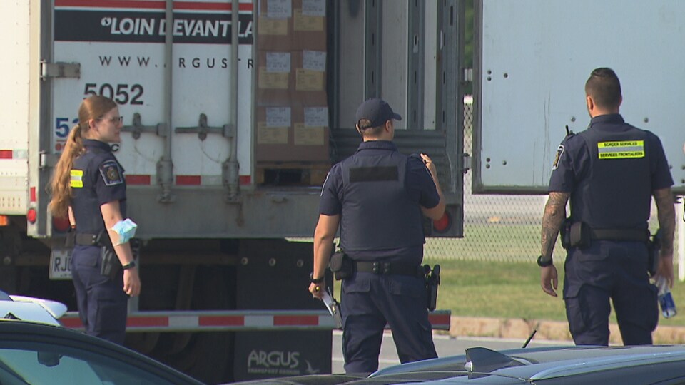 Quatre agents des services frontaliers fouillent un camion.