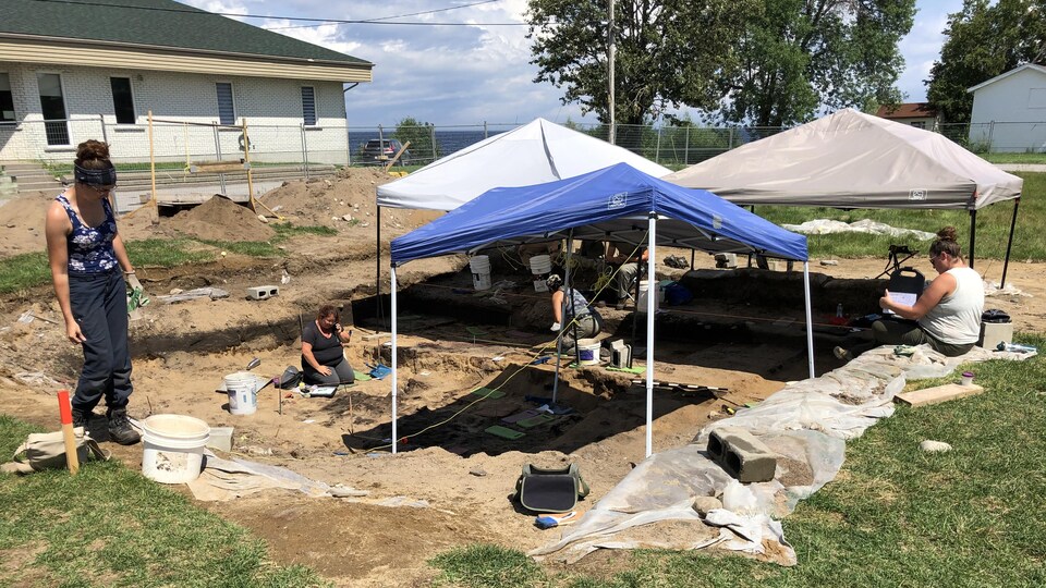 Des personnes fouillent un site archéologique sous des tentes pare-soleil.