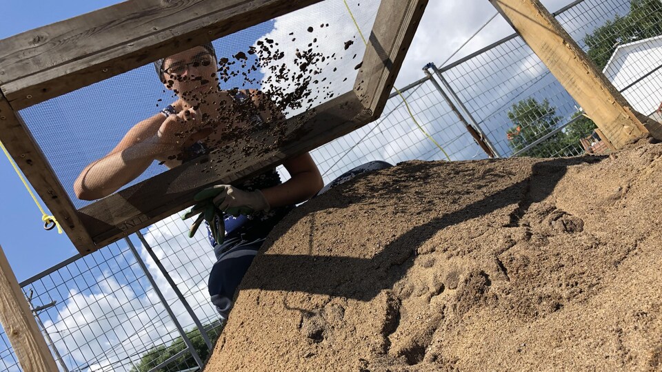 Hélèna Launière en train de tamiser des objets au-dessus d'un bac de sable.