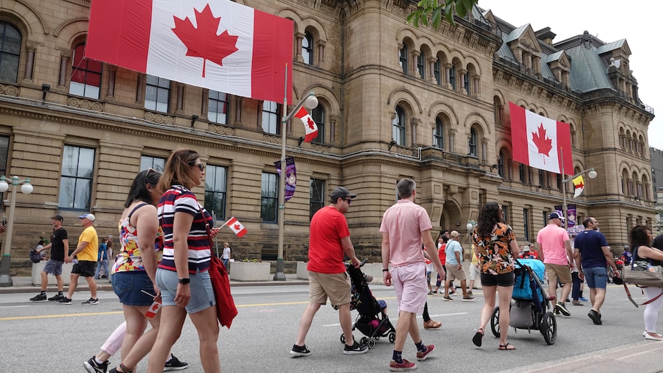 Plusieurs personnes marchent sur la rue Wellington devant des drapeaux géants du Canada, installés sur la façade d'immeubles.