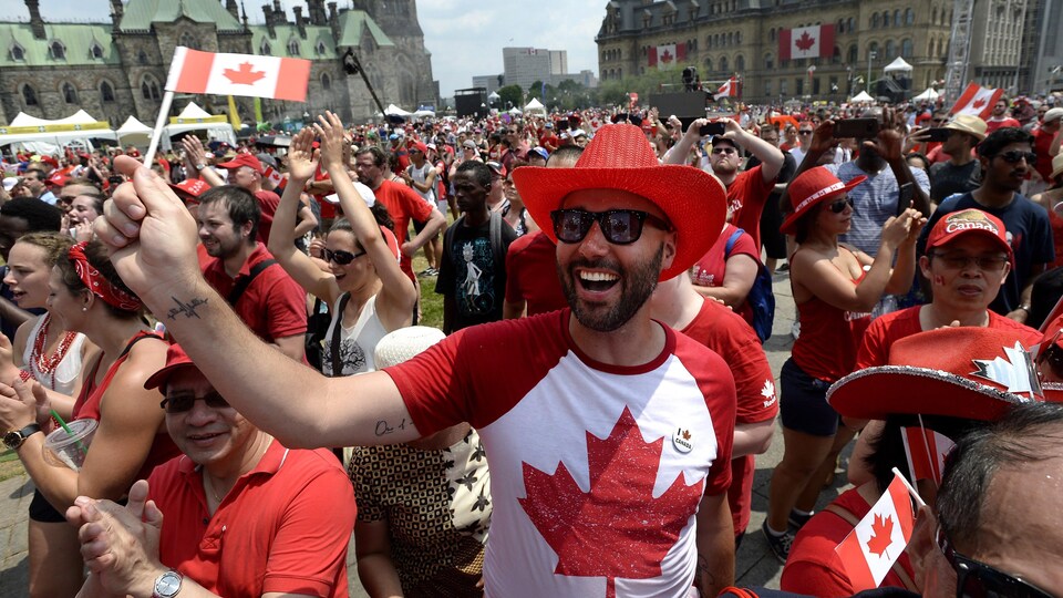 Des gens habillés de rouge et blanc agitent des drapeaux du Canada sur la colline du Parlement.