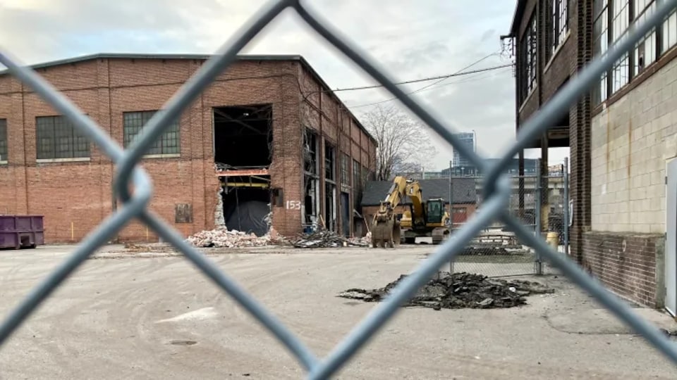 Un vieux bâtiment en briques dont certains pans ont été défaits, de la machinerie est visible tout près.