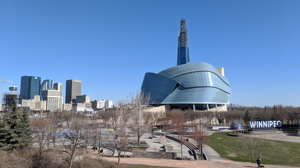 Le Musée canadien pour les droits de la personne vu de l'extérieur entouré d'espaces verts, avec des bâtiments du centre-ville de Winnipeg en arrière-plan.