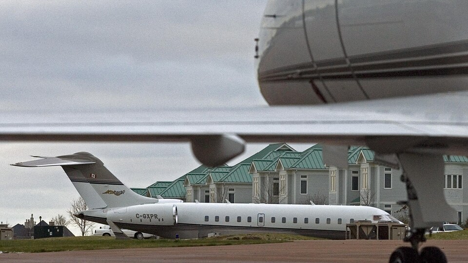 Un jet privé posé sur une piste d'atterrissage avec des résidences à l'arrière-plan.