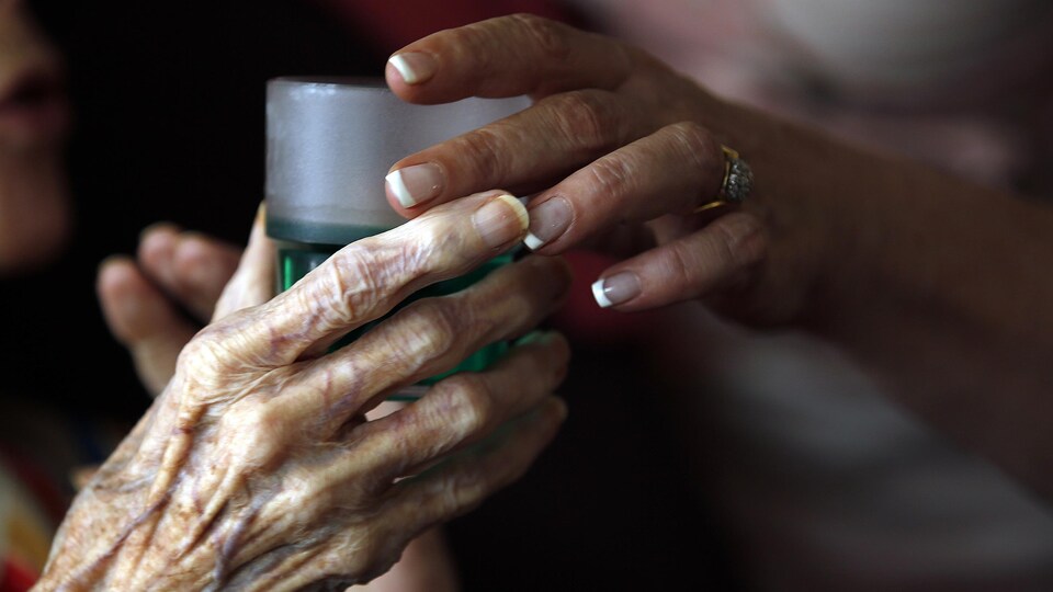 Plan rapproché de la main d'une femme âgée qui saisit un verre rempli de liquide vert.