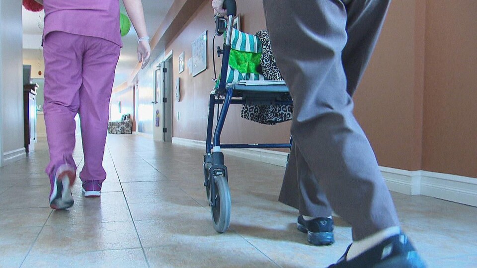 Les jambes d'une employée de foyer de soins et d'un homme poussant une marchette.