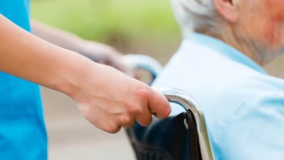 Une préposée aux soins aide un patient à se déplacer en fauteuil roulant