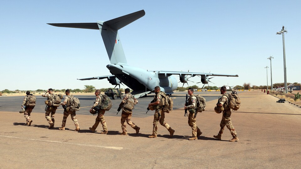 Des militaires français marchent sur le tarmac d'un aéroport où se trouve un avion.