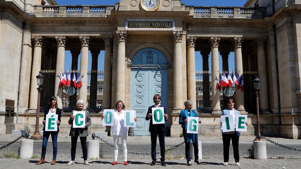 Cinq hommes et une femme tiennent les lettres formant le mot Écologie sur le pavé devant l'Assemblée nationale. 