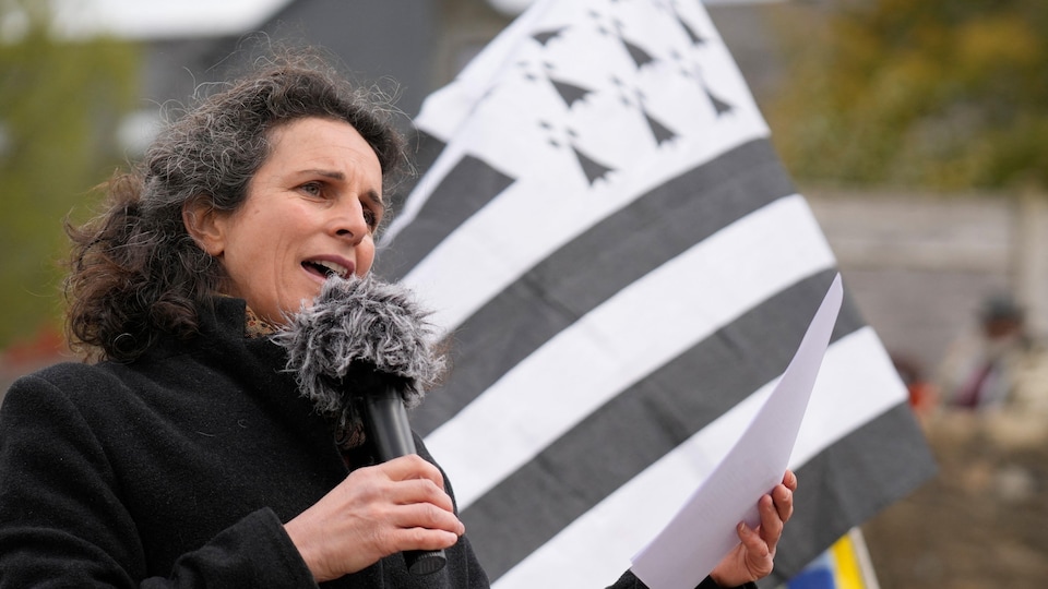 Morgan Large tient un micro devant un drapeau breton.