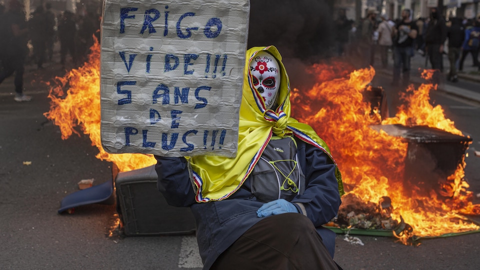 Un manifestant tient une banderole sur laquelle on peut lire Frigo vide à une barricade en feu lors d'une marche marquant la Journée internationale des travailleurs, le 1er mai 2022, à Paris.