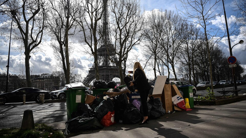 Une femme dépose un sac à ordures sur des conteneurs d'ordures ménagères non collectés devant la tour Eiffel à Paris le 15 mars 2023.