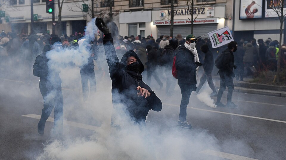 Un homme devant une foule de manifestants lance un projectile.