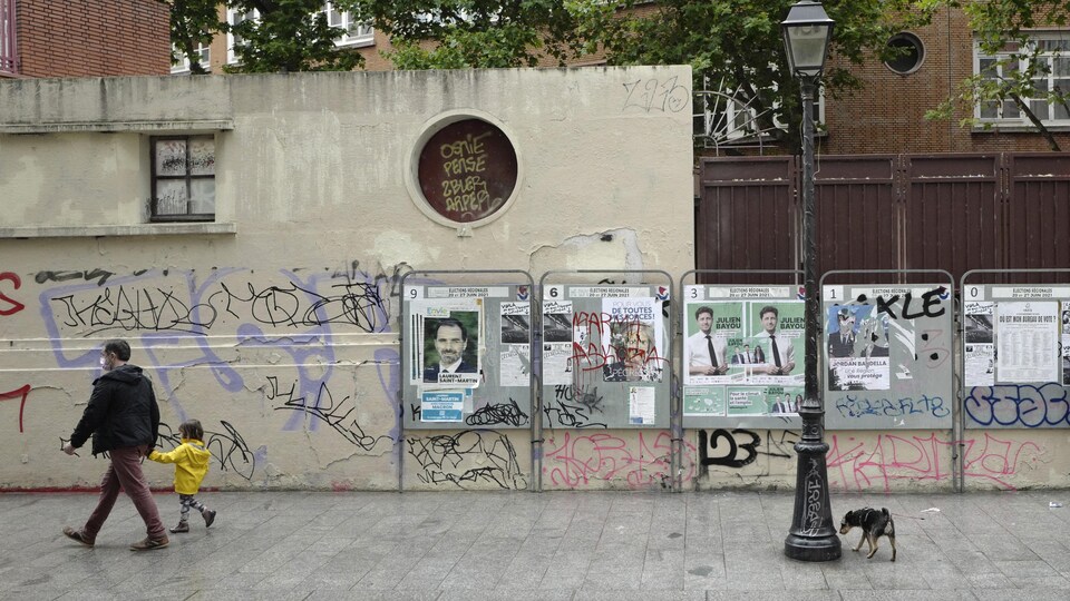Un homme et un enfant marchent le long d'un mur couvert de graffitis et d'affiches de candidats