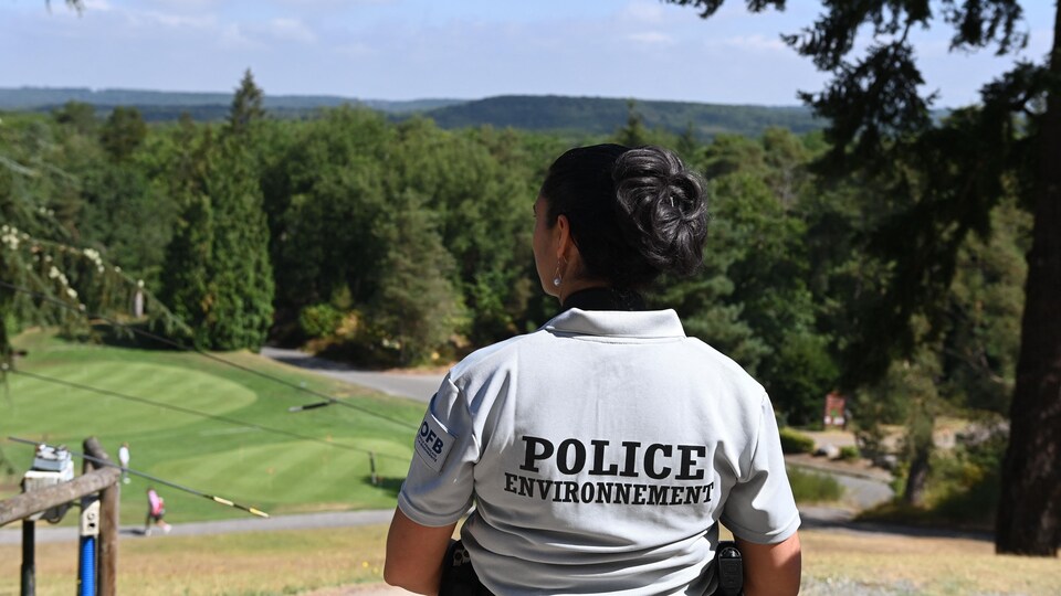 Une femme vêtue à l'effigie de la police environnementale regarde un terrain de golf.
