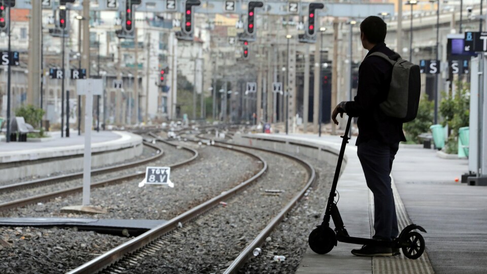 Un jeune avec sa trottinette sur le quai d'une gare.