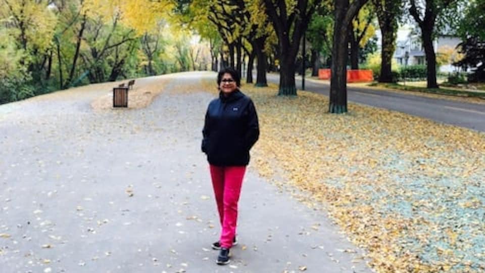 Frances Sreedhar sur un chemin bordé d'arbres à l'automne avec les feuilles qui ont commencé à tomber.