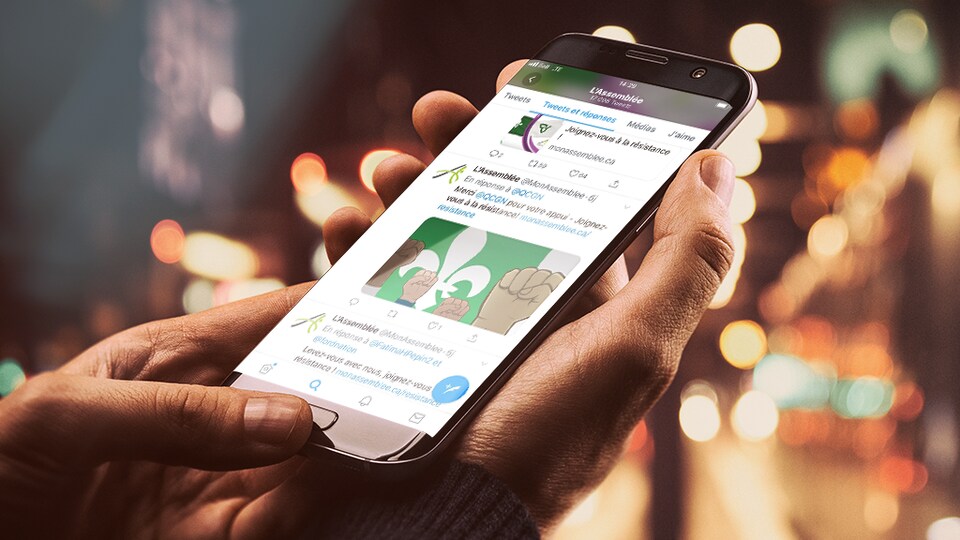 Dans une main, l'écran d'un téléphone intelligent affichant une page Twitter d'un organisme franco-ontarien