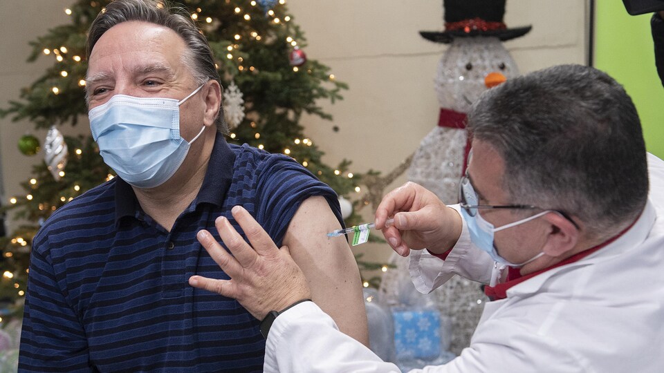 François Legault reçoit un vaccin. On peut voir le vaccinateur à droite.