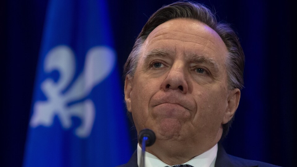Gros plan sur le visage de François Legault, la bouche pincée devant un micro.