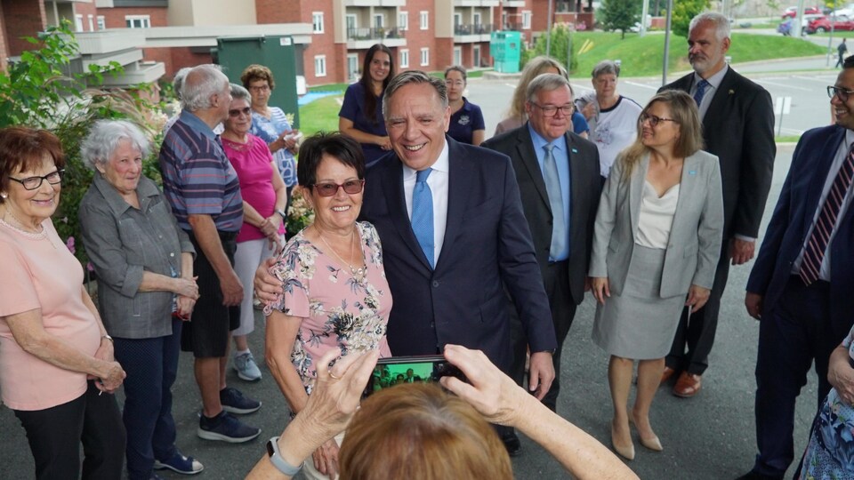 François Legault pose avec une dame pour une photo, tandis que plusieurs personnes les entourent.