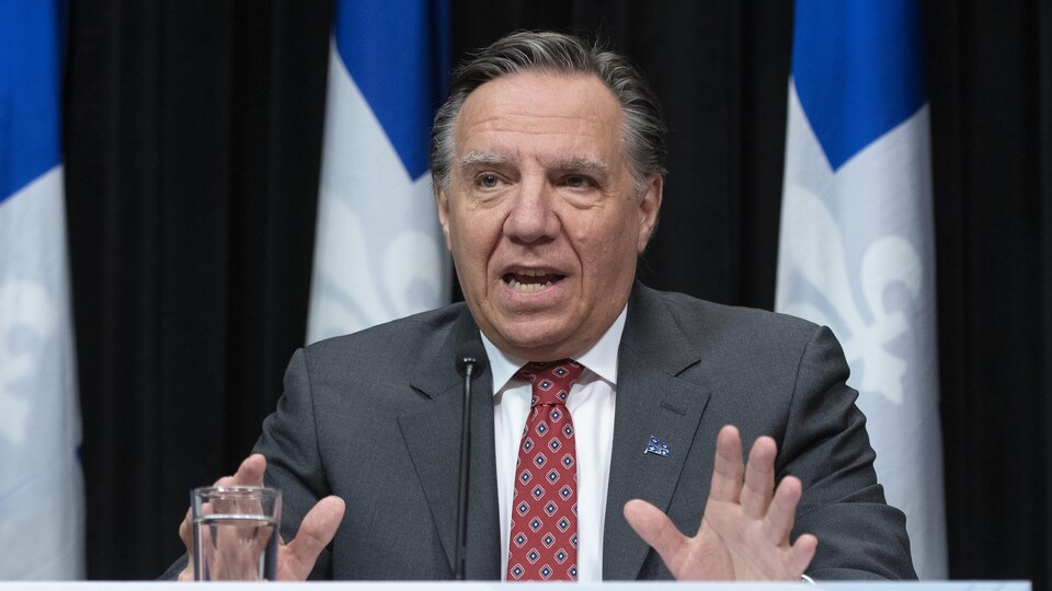 Le premier ministre parle devant des drapeaux du Québec.