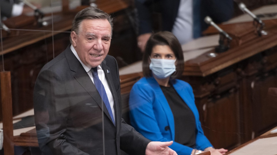 François Legault prononce un discours, debout à l'Assemblée nationale, tandis que Geneviève Guilbault l'écoute assise, portant un masque.