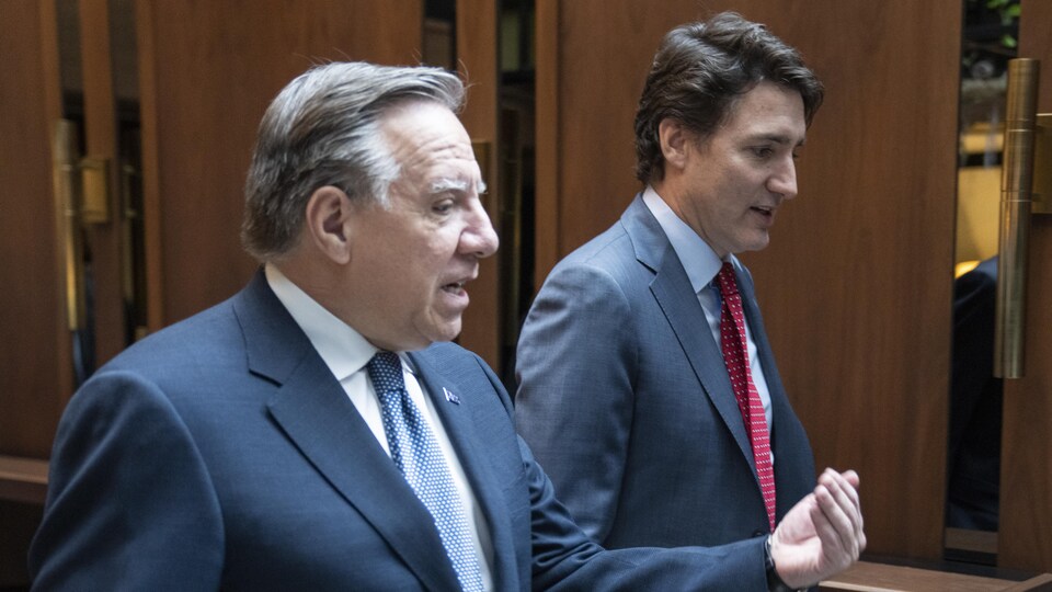 François Legault et Justin Trudeau marchent dans un corridor orné de boiseries.