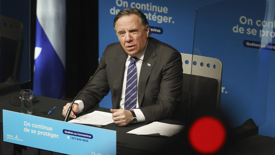 François Legault parle au micro, assis derrière un bureau.