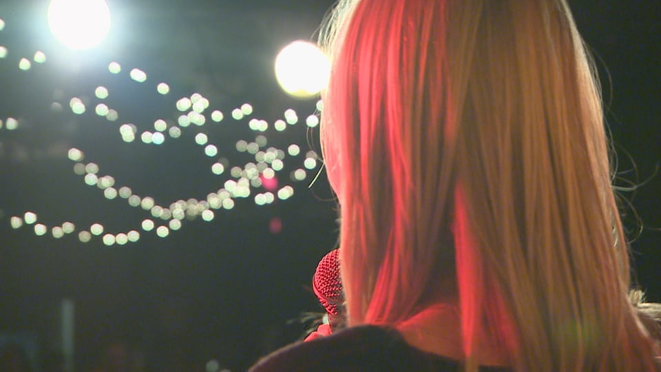 Une chanteuse qui tient un micro devant une foule dans la noirceur et des petites lumières.