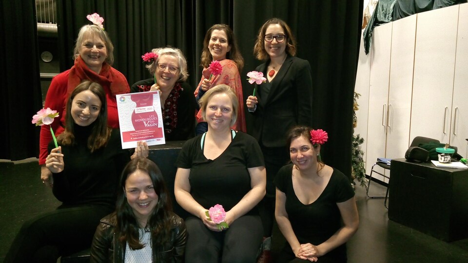 Une groupe de 8 femmes posent une fleur rose à la main ou dans les cheveux.