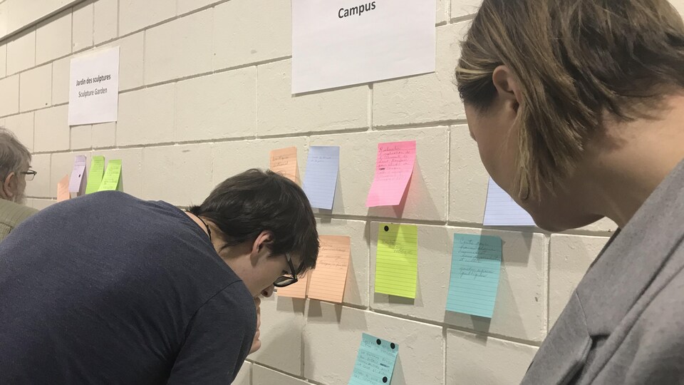 Des gens regardent un mur où il y a des papiers collés.