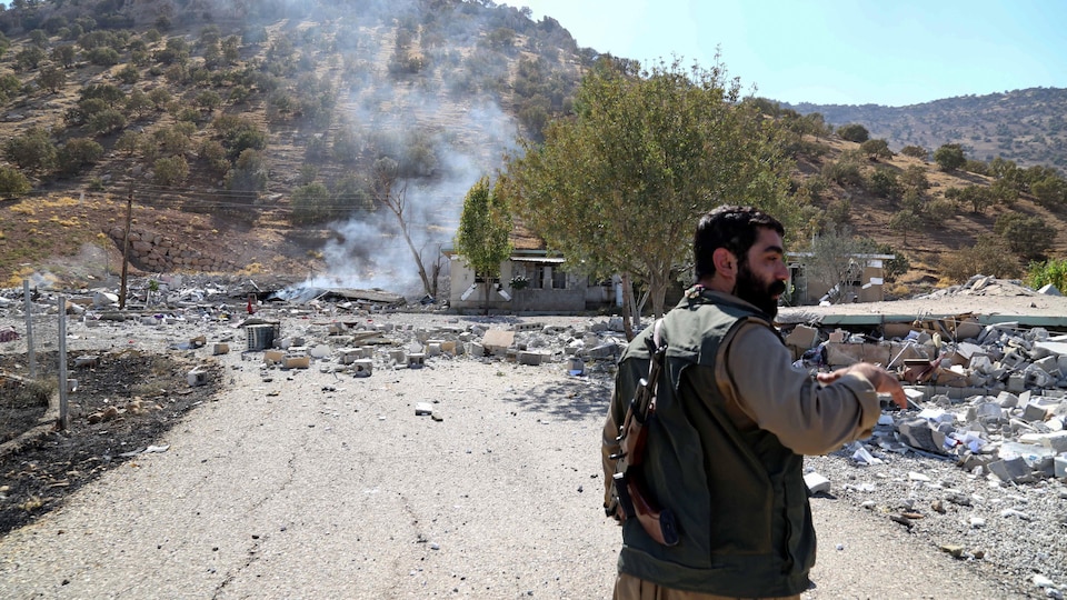 Un militaire kurde devant les décombres d'une maison et de la fumée. 