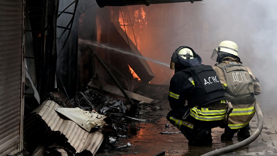 Deux pompiers accroupis tentent d'éteindre un incendie.