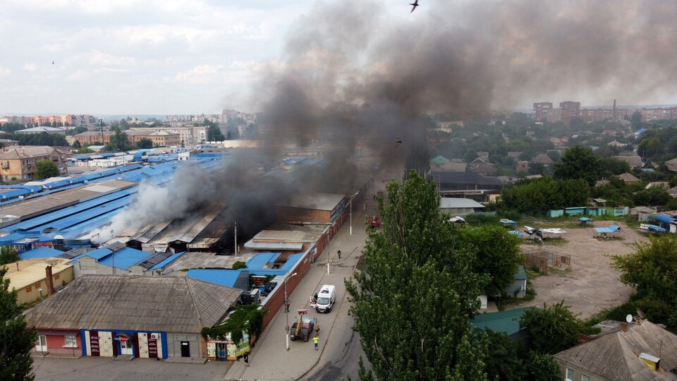 Vue aérienne d'un marché, d'où s'échappe une colonne de fumée.