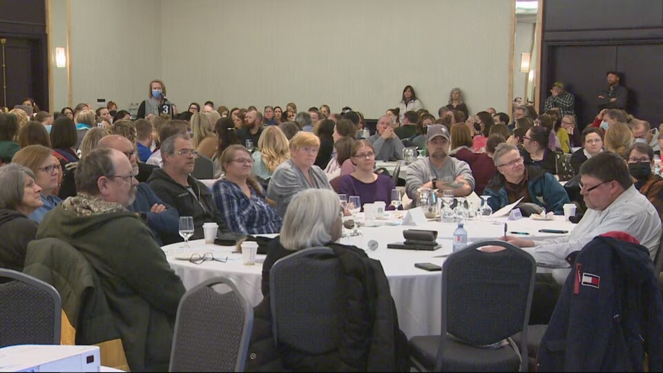 Une foule assise à des tables dans une grande salle de conférence.