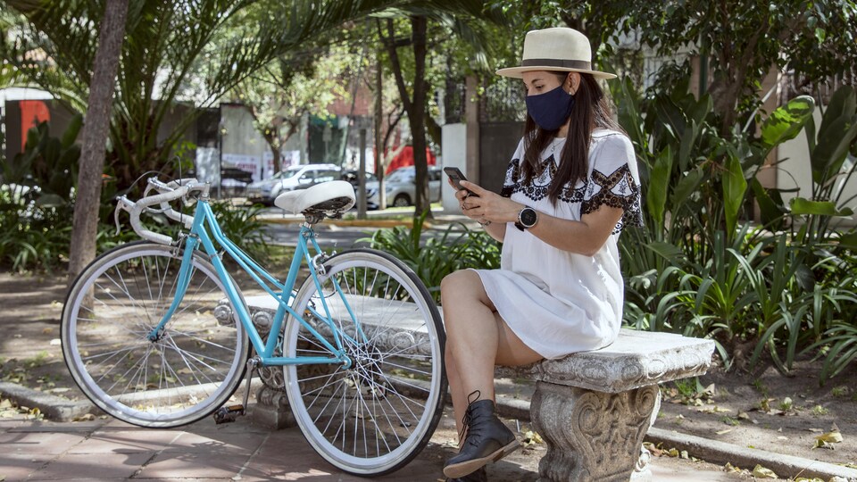 Une femme regarde son téléphone intelligent sur un banc au Mexique, à côté de son vélo.