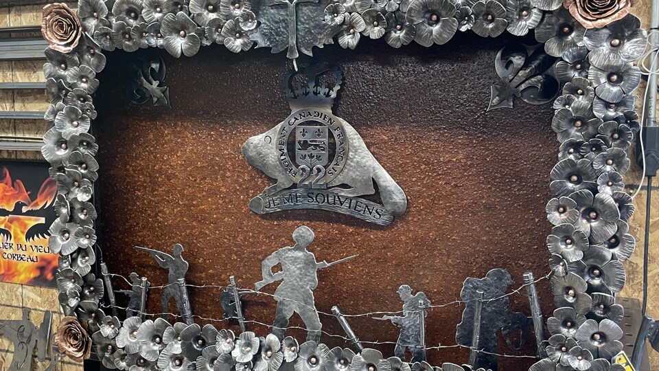 La fresque comporte des dizaines de coquelicots en acier. Au centre, des soldats au combat avec un fil barbelé et l'écriture Je ms souviens. 
