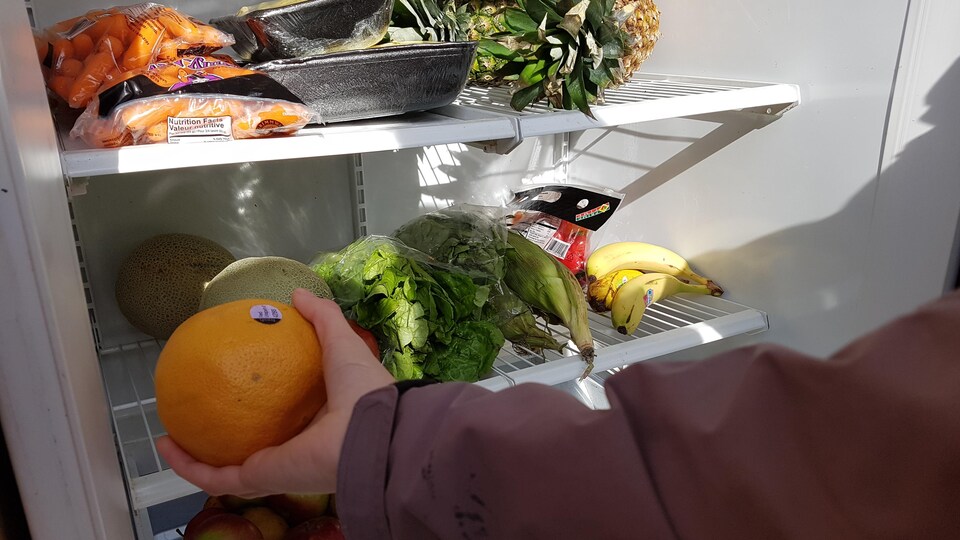 Une main tendu vers une orange dans un frigo