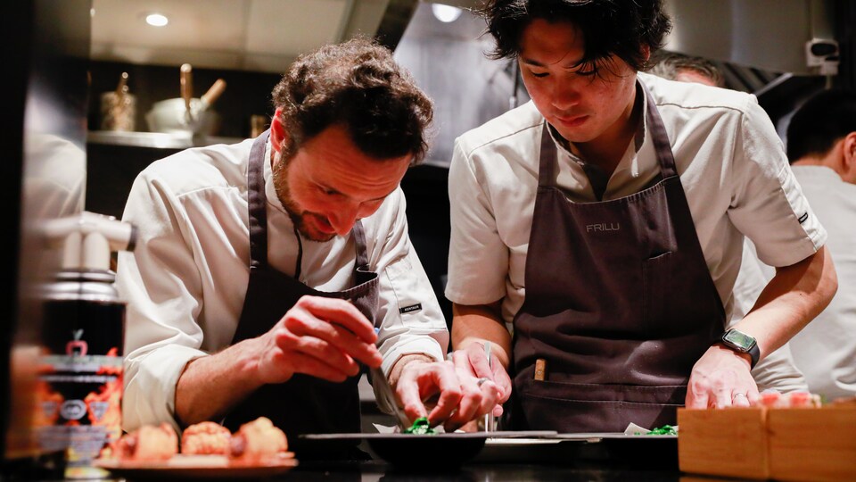 Le chef John-Vincent Troiano et son second So Sakata penché sur des assiettes sur le plan de travail de la cuisine du restaurant.
