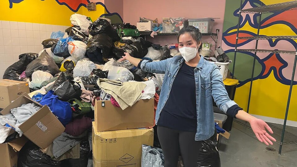 Une personne pose devant des boîtes et sacs remplis de dons.
