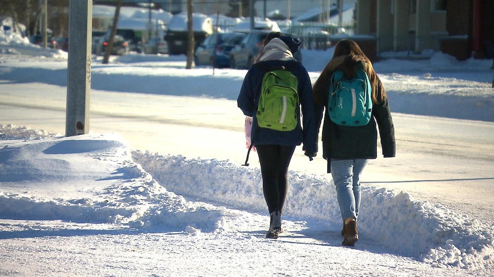 Deux jeunes filles marchent côte à côte sur un trottoir enneigé.