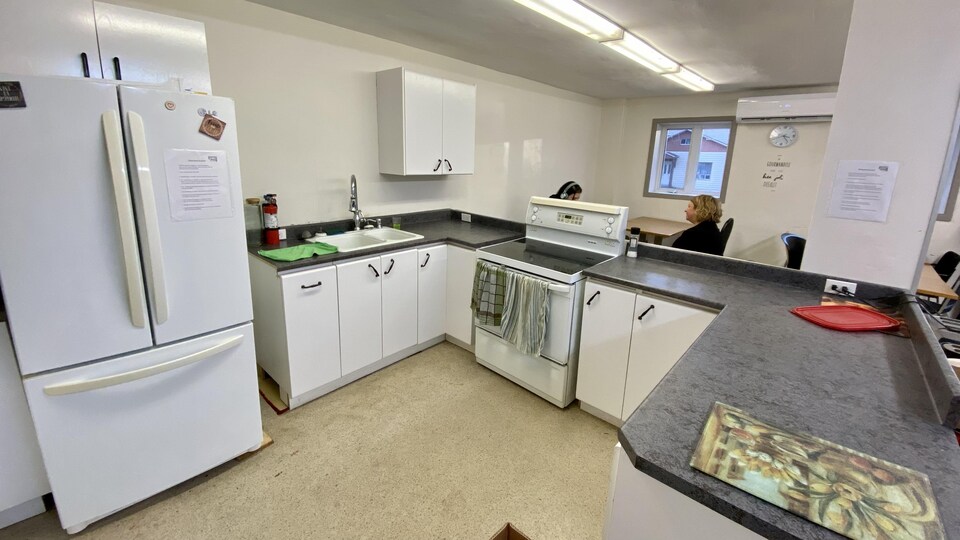 Des armoires, un évier, un réfrigérateur, une cuisinière et un comptoir sont disposés devant une table et des chaises.  
