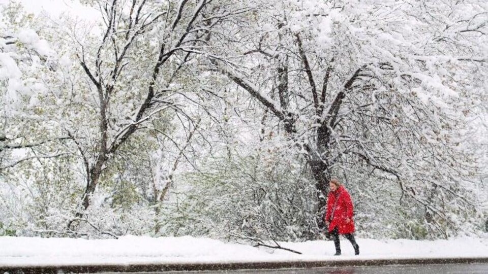 Une femme dans un manteau rouge marche dehors alors que la neige tombe et que tout est couvert de blanc.