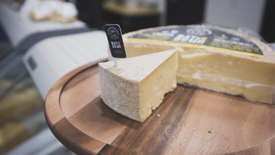 Une pointe de fromage croûté est posée sur une planche de bois.