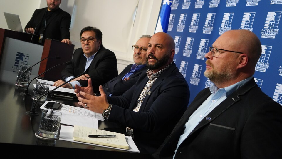 Quatre représentants syndicaux assis derrière une table durant une conférence de presse.